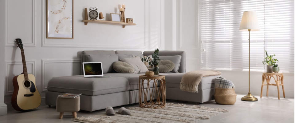 Modern living room with a gray sectional sofa, acoustic guitar, laptop, and decorative accents, visually illustrating how insurance rates are determined by evaluating the value of personal belongings.