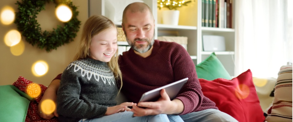 Father and daughter sitting on a festive couch looking at a tablet for renters insurance options to enhance safety during holidays.