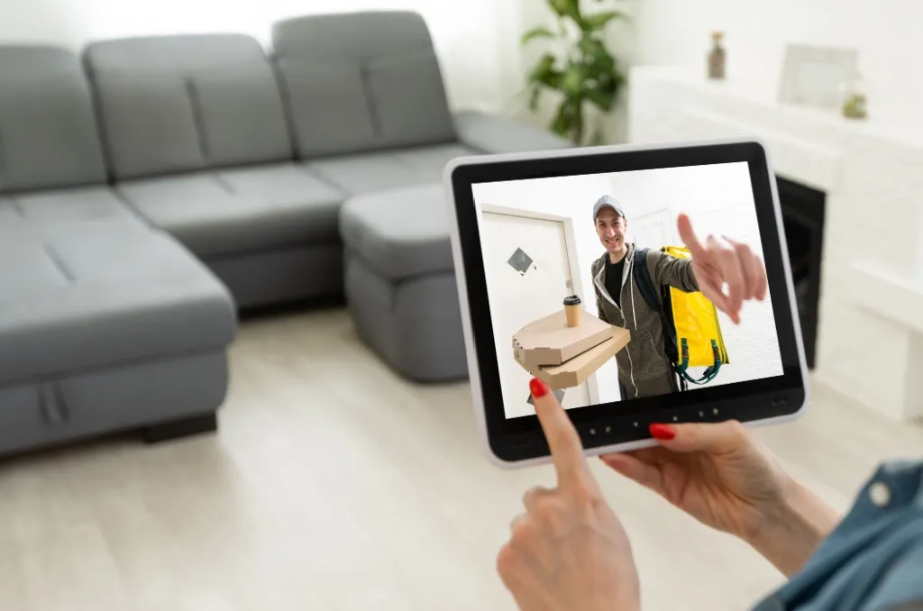 A person using a smart home tablet in a cozy living room to view a delivery person at the front door, illustrating how renter-friendly security systems provide extra peace of mind and convenience.