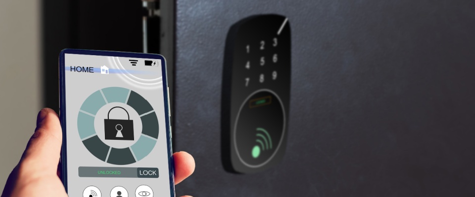 A person holds a smartphone displaying a home security app in front of a smart door lock with a touchscreen keypad, as a renter-friendly security system.