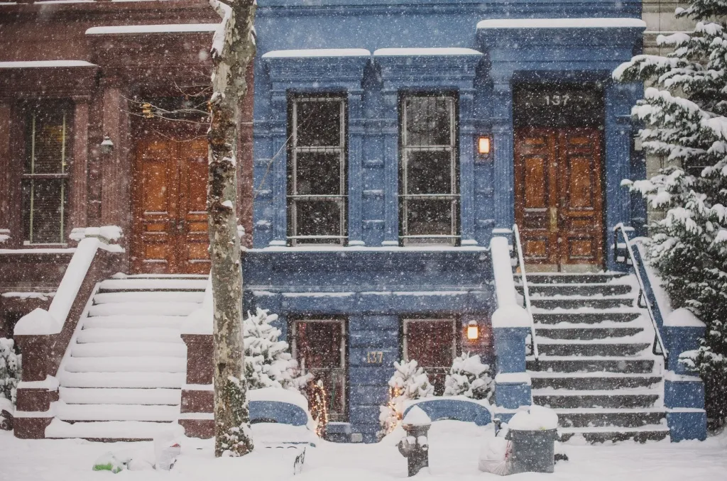 Snow-covered row houses and icy steps during a storm, reinforcing the importance of snow shoveling safety for walkways and entrances.
