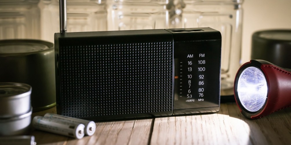 Battery-powered radio, flashlight, and extra batteries displayed on a wooden table, demonstrating essential items to include in a power outage emergency kit.