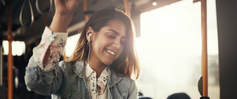 Young woman riding public transportation with earphones, holding onto an overhead rail, visually illustrating important questions to ask before signing a lease, such as considering the daily commute.