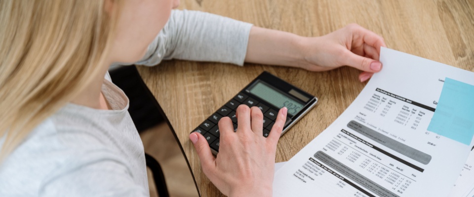 Woman reviewing utility bills and using a calculator at a wooden table, in order to ask better questions before signing a lease about total monthly costs.