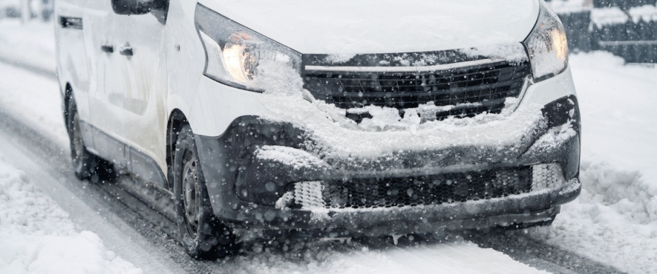 Delivery van driving through heavy snowfall, illustrating why planning your deliveries ahead is important when learning how to prepare for a winter storm in an apartment.