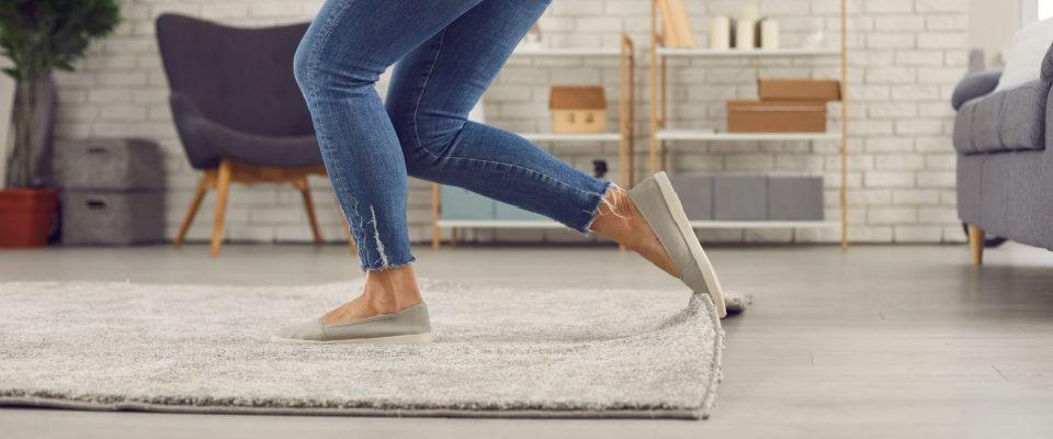 Person tripping over a curled edge of a rug in a modern living room, visually representing renters insurance mistakes such as underestimating liability risks and not having adequate coverage for accidents in an apartment.