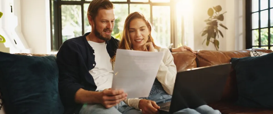 Couple sitting on a couch reviewing documents and online policies, learning how high-value item coverage protects their most important belongings.
