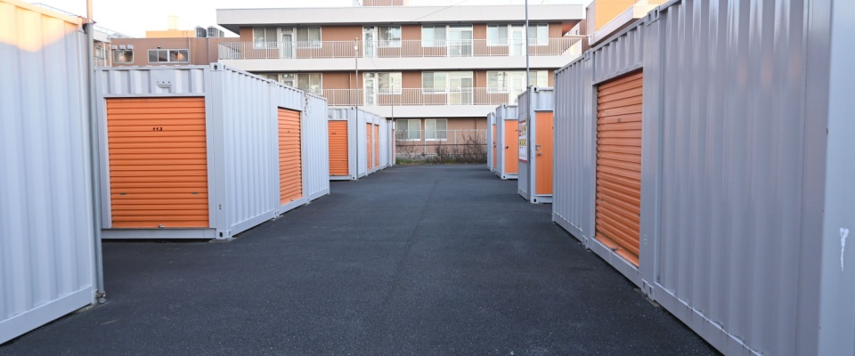 Row of outdoor storage units with orange roll-up doors in a secure facility, which have certain renters insurance coverage.