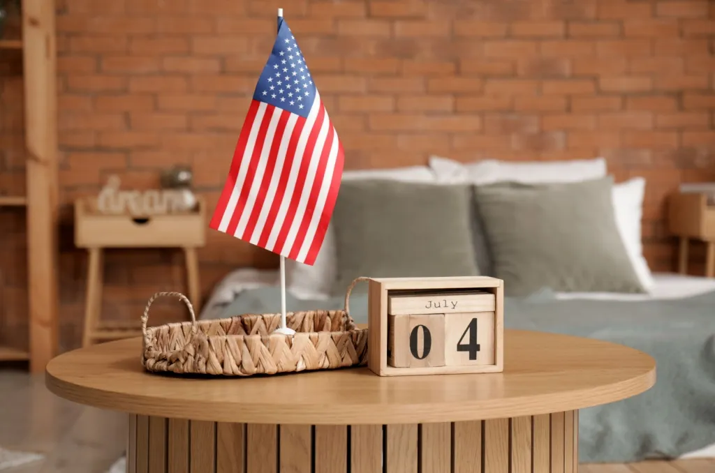 Wooden table with a small American flag and a calendar block displaying July 4th in a cozy bedroom, serving as a reminder for 4th of July safety tips in an apartment.