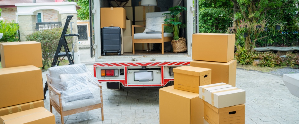 Moving truck parked in driveway with cardboard boxes, furniture, and household items being loaded or unloaded, illustrating the benefits of renters insurance coverage during moving.