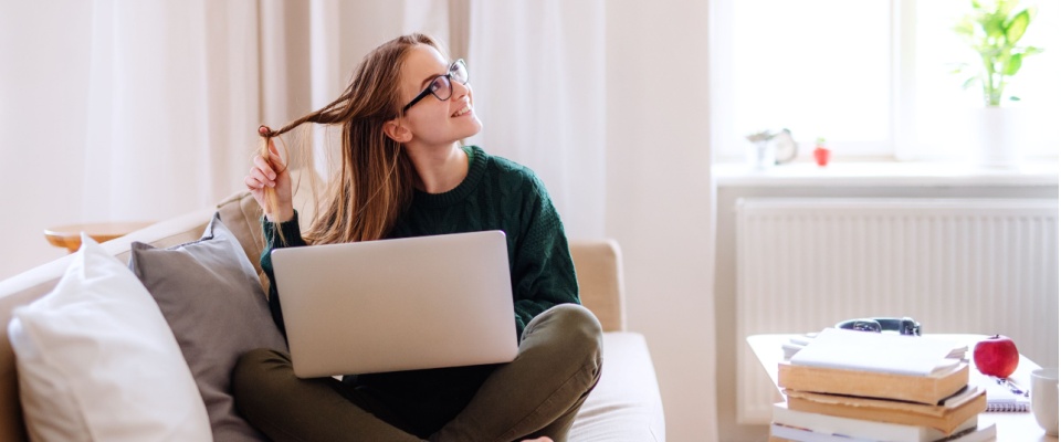 College student sitting cross-legged on a sofa with a laptop and textbooks in a bright apartment, while checking student renters insurance options.