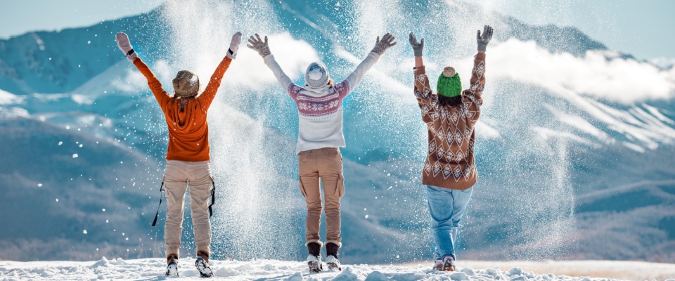 Group of people playing in the snow with mountains in the background, representing outdoor fun and cold-weather winter vacation safety.