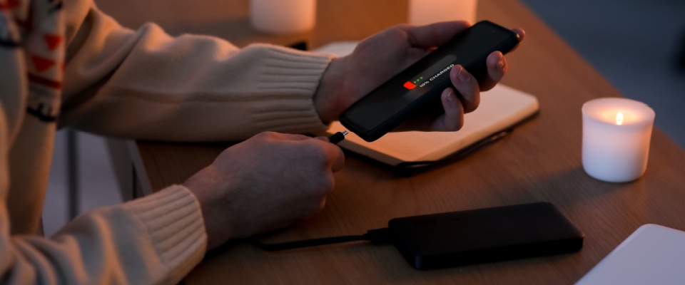 Person charging phone with a power bank surrounded by candles, showing how to winterize your apartment by preparing for potential power outages.