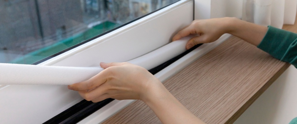 Hands applying insulation to a window frame, demonstrating how to winterize your apartment and prevent drafts during cold months.
