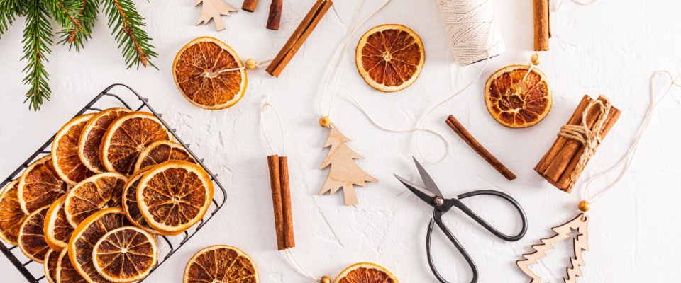 Flat lay of dried orange slices, cinnamon sticks, twine, and scissors arranged for creating a festive DIY holiday decoration.