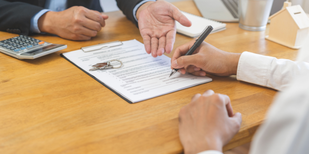 A renter sitting at a desk, holding a pen, and signing a lease agreement that includes a clause for renters insurance required by the landlord.