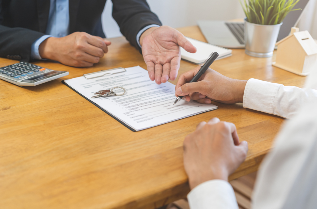 A renter sitting at a desk, holding a pen, and signing a lease agreement that includes a clause for renters insurance required by the landlord.