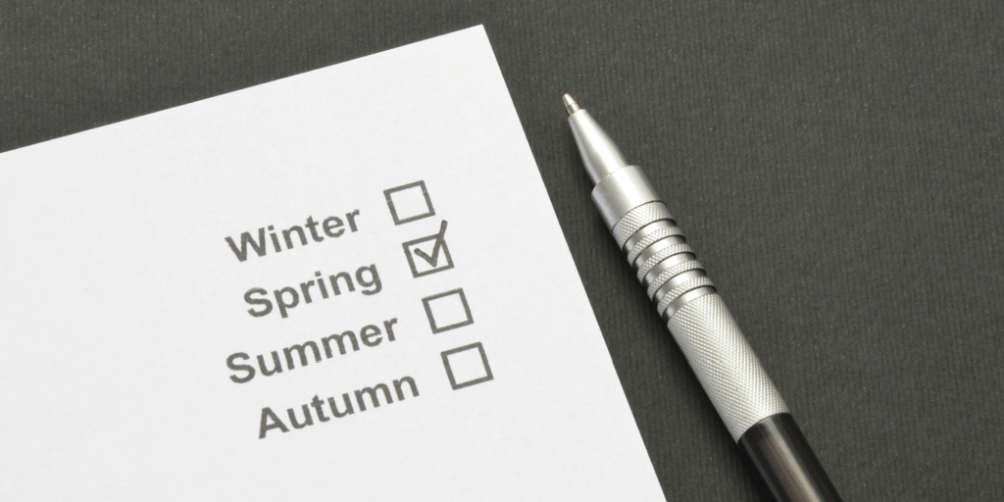 Cleaning checklist for seasonal organization with a marked checkbox for 'Spring' on white paper next to a silver pen.