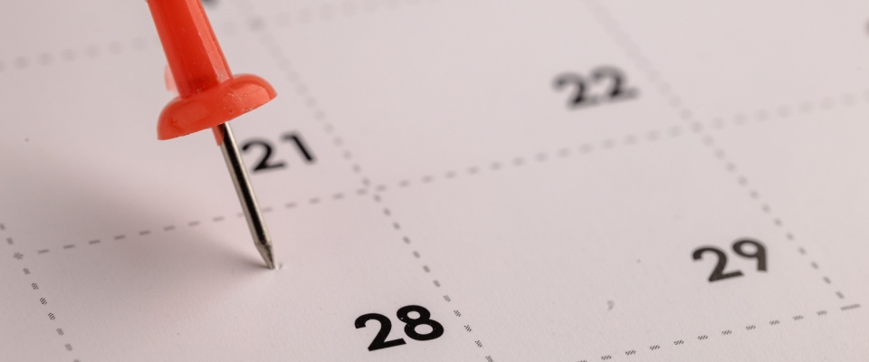 A close-up of a calendar with a red pushpin marking a specific date near the end of the month, highlighting the best time to start searching for an apartment.
