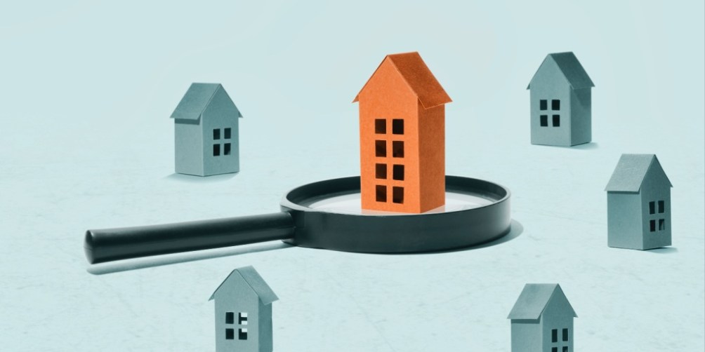 Illustration of a magnifying glass highlighting a standout orange house among grey houses, symbolizing the search for the best time to rent an apartment.