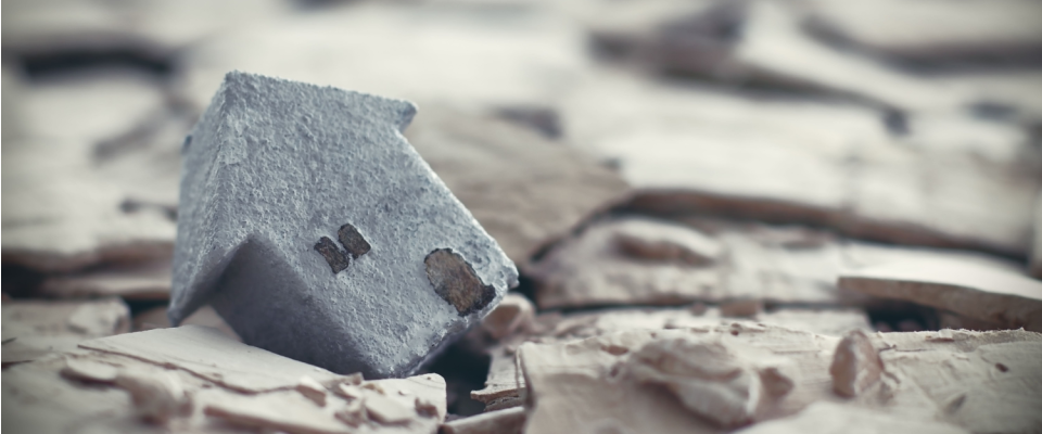 Close-up of a small house model on dry ground, highlighting what renters insurance doesn't cover, such as natural disasters and structural damage.