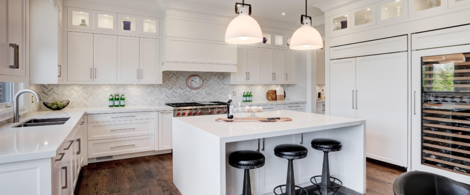 Clean and stylish white kitchen featuring a countertop island, hanging lights, storage cabinets, and appliances in good condition, where following electrical safety tips helps prevent accidents.