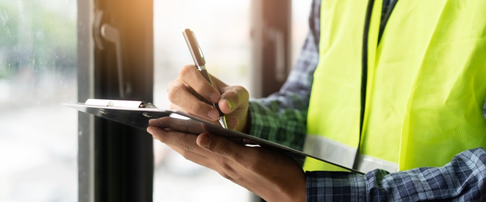 Inspector wearing a yellow safety vest and holding a clipboard, documenting details during an energy efficiency assessment.