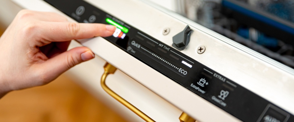 person pressing the eco mode button on a modern dishwasher, highlighting its Energy Star efficiency rating and showcasing how energy-efficient appliances help reduce electricity consumption in the home.