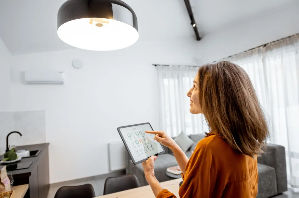 Woman using a tablet to control energy-saving devices in a modern, well-lit living room.