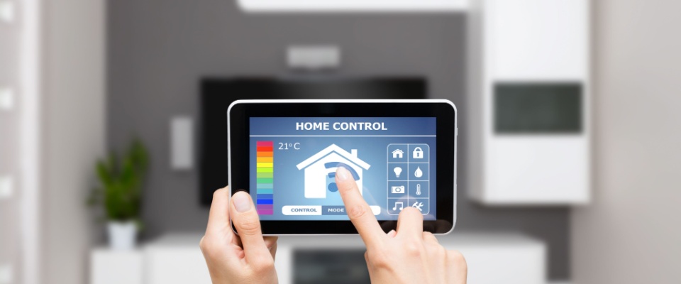 Person holding a tablet displaying a home control app in a modern living room, demonstrating the use of energy-saving devices like smart thermostats and automated monitoring systems.