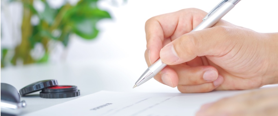A guarantor or a cosigner signing a rental agreement with a pen, at a white desk.