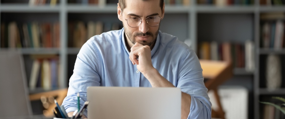Man in a light blue shirt sitting at a desk with a laptop and paperwork in a home office, illustrating renters insurance mistakes such as not filing a claim in due time.