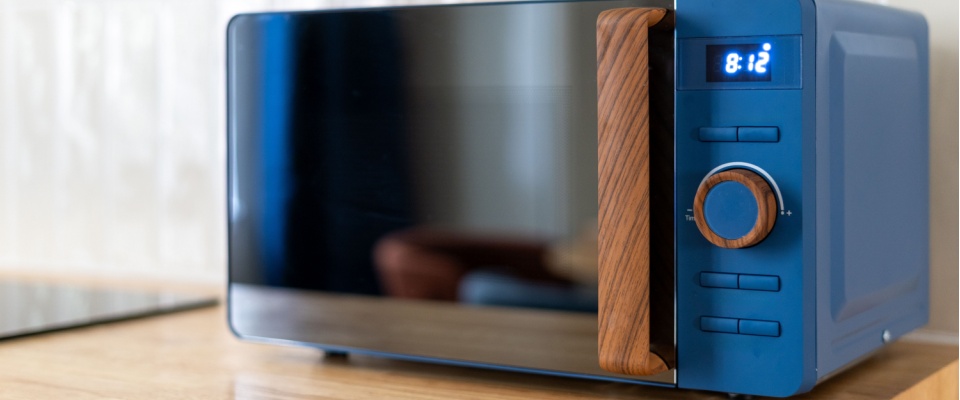 Modern black microwave with a digital clock on a wooden countertop, illustrating the concept of unplugging appliances to save electricity by preventing phantom energy use.