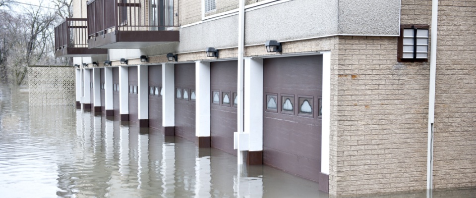 Row of garage doors partially submerged in floodwater outside an apartment building, illustrating a situation in which renters insurance doesn't cover flooding.