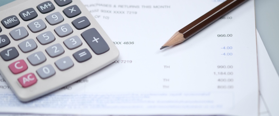 A calculator and pencil rest on top of printed utility bills and financial documents, helpful when comparing electricity plans.