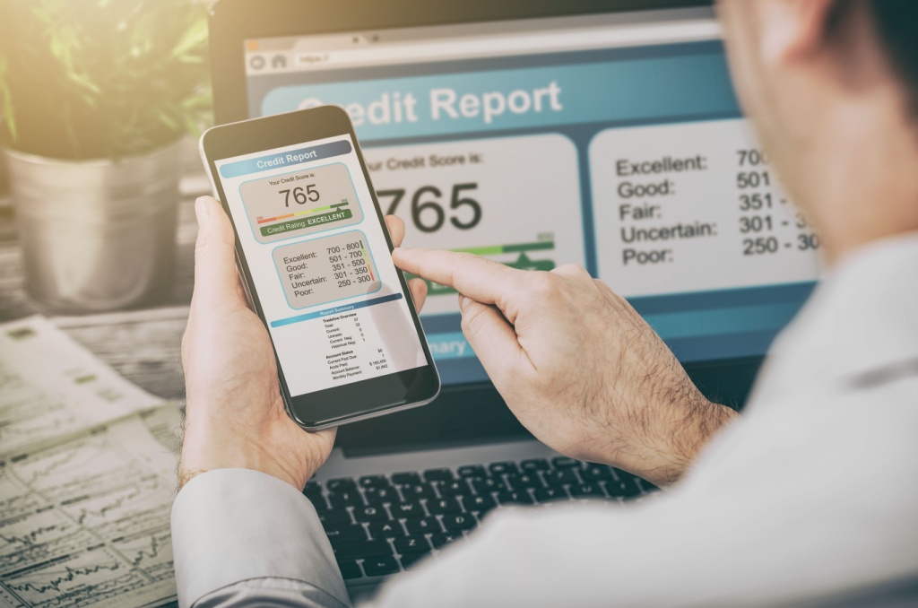 A person reviewing their credit score of 765 on a smartphone and laptop, while the question of "does renters insurance affect credit score?" might be on their mind.