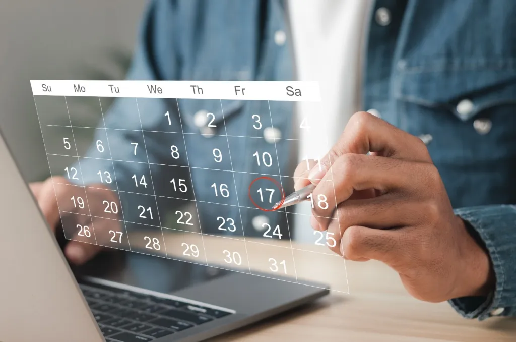 Person holding a pen and marking the effective date for their renters insurance policy on a transparent calendar overlay while working on a laptop.
