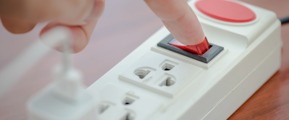 Person turning on a white power strip with a mobile phone charger plugged in, after a power outage.