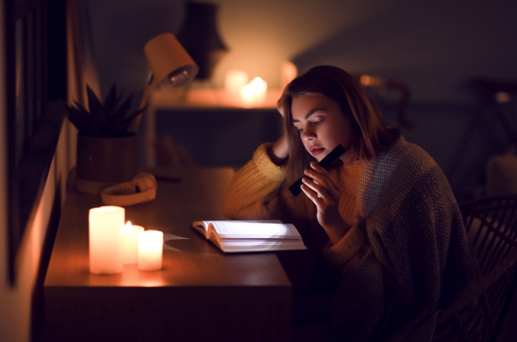 Woman using a flashlight and candles to read a book during a blackout, showing how to stay calm and prepared when the power goes out.