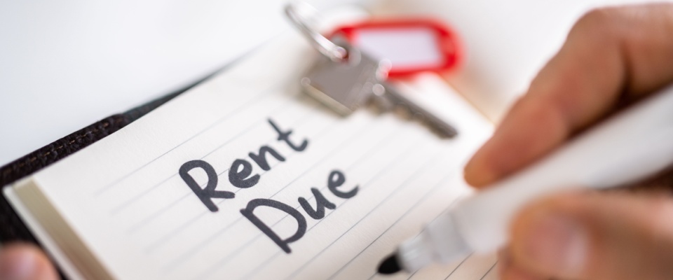 Close-up of someone writing ‘Rent Due’ beside house keys, illustrating how unpaid rent after moving out of an apartment could impact credit score.