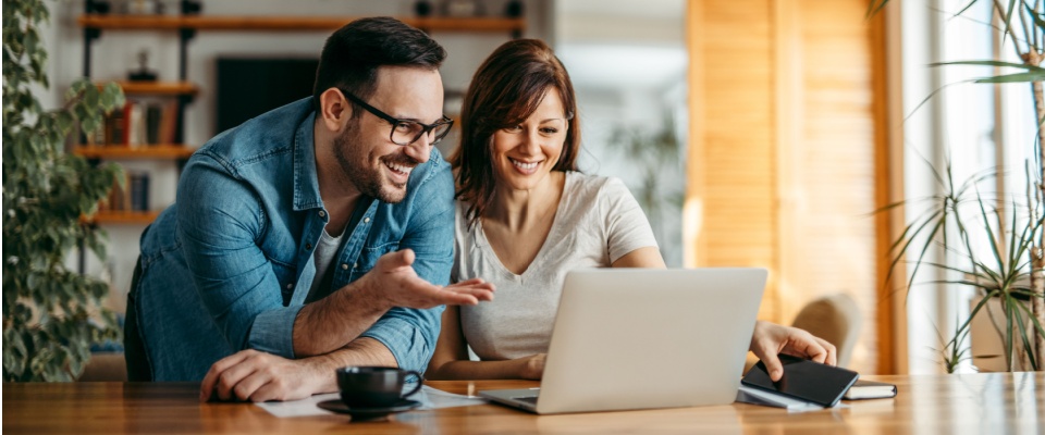 Couple sitting at a table reviewing documents on a laptop, working together to compare renters insurance policies and coverage options.