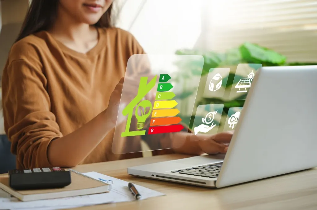 Person using a laptop with a digital energy efficiency rating graphic, highlighting the role of a home energy audit in reducing utility costs.