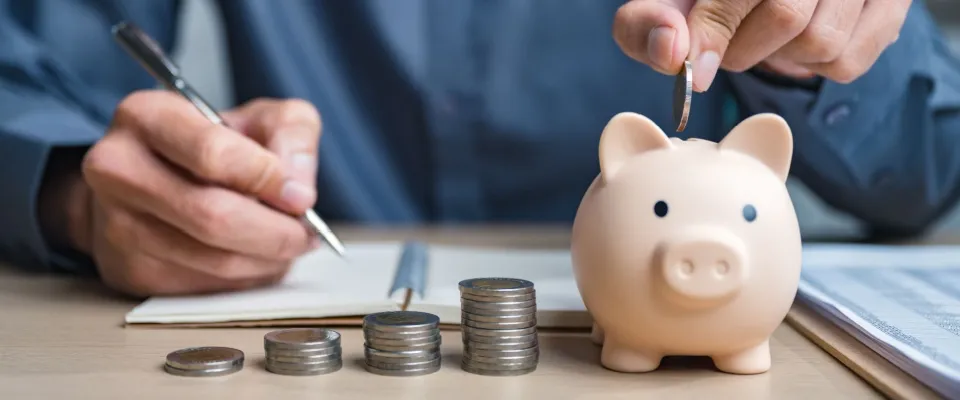 Person placing coins into a piggy bank next to a calculator, planning savings while determining how much of income should go to rent.