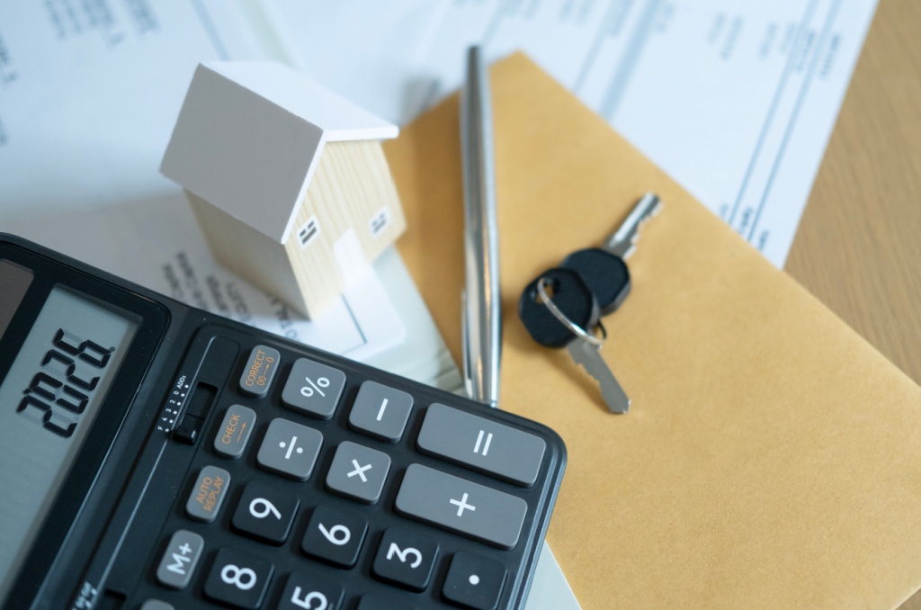 Calculator, house model, and keys on paperwork, representing financial planning decisions about how much of income should go to rent.