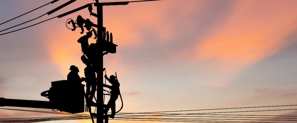 Electric utility workers servicing power lines at sunset, showing labor and grid maintenance covered by TDU delivery charges.