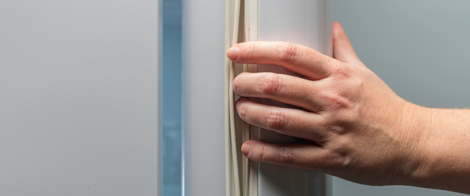 Appliance maintenance involving a hand inspecting the rubber door gasket seal of a refrigerator.