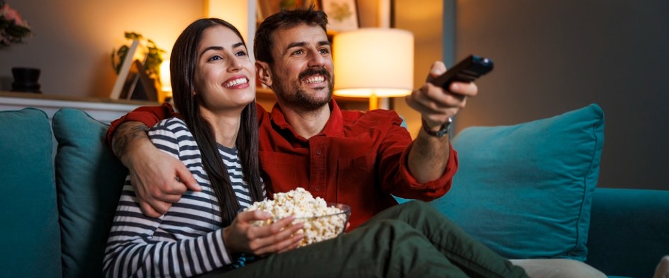 Couple relaxing on the couch, watching TV and sharing popcorn, highlighting home entertainment and streaming with RentCafe Internet.